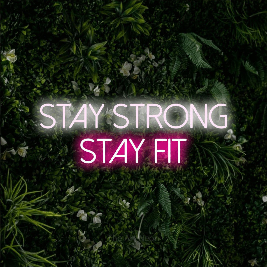 Enseigne néon à DEL à lumière rose vif et blanche froide, affichant « Stay Strong Stay Fit » sur un mur de feuillage vert, pour décorer une salle d’entraînement