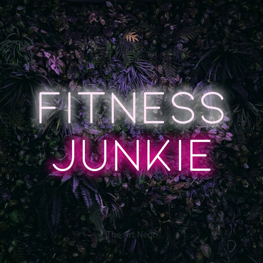 Hot pink and cool white LED neon sign reading "Fitness Junkie" against a purple floral wall for gym décor