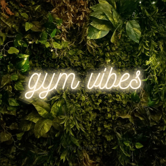 Warm white script-style LED neon sign reading "Gym Vibes" against a textured moss and foliage wall for gym décor