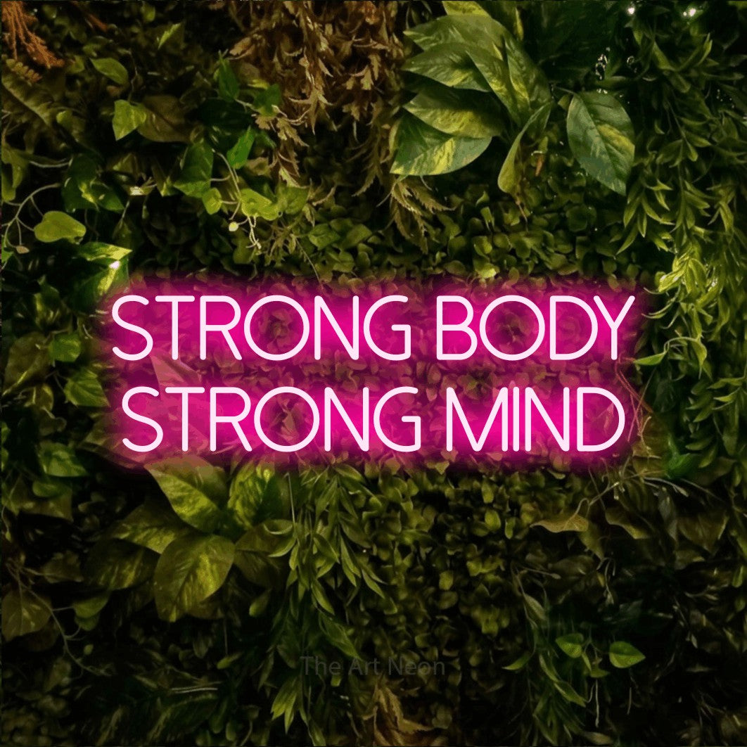 Enseigne néon à DEL à lumière rose vif, affichant « Strong Body Strong Mind » sur un mur texturé de mousse et de feuillage, pour décorer une salle d’entraînement