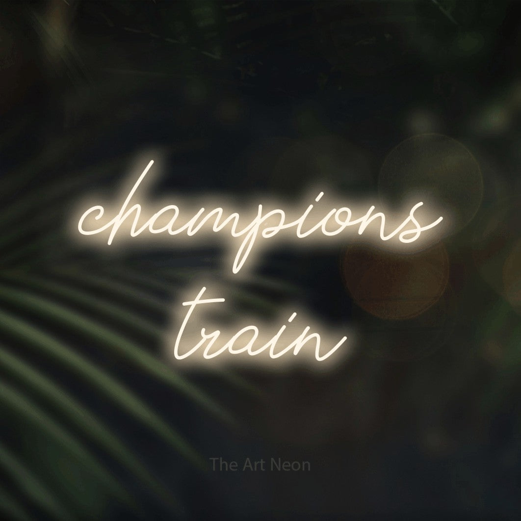 Warm white script-style LED neon sign reading "Champions Train" against dark blurred palm leaves for gym décor