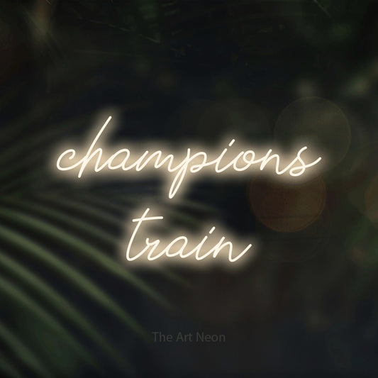 Enseigne néon à DEL à lumière blanche chaude, de style manuscrit, affichant « Champions Train » sur des feuilles de palmier foncées et floues, pour décorer une salle d’entraînement