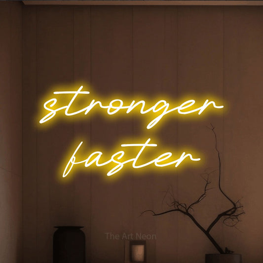 Enseigne néon à DEL à lumière jaune, affichant « Stronger Faster » sur un mur brun chaleureux, pour décorer une salle d’entraînement
