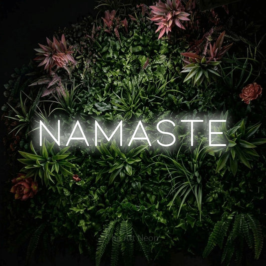 Cool white LED neon sign reading "Namaste" against a flowering garden wall for gym décor
