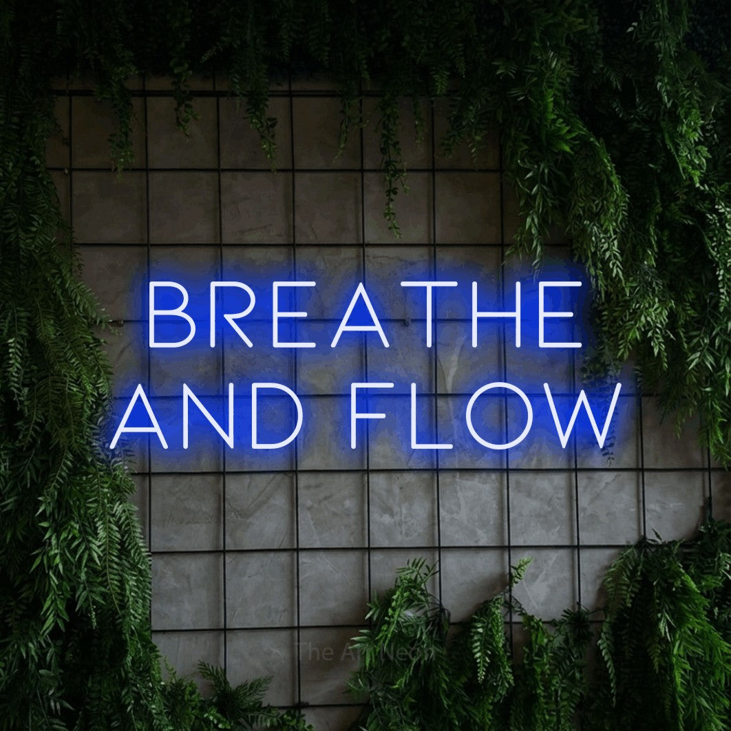 Enseigne néon à DEL à lumière bleue, affichant « Breathe and Flow » sur un mur quadrillé vert avec du feuillage, pour décorer une salle d’entraînement