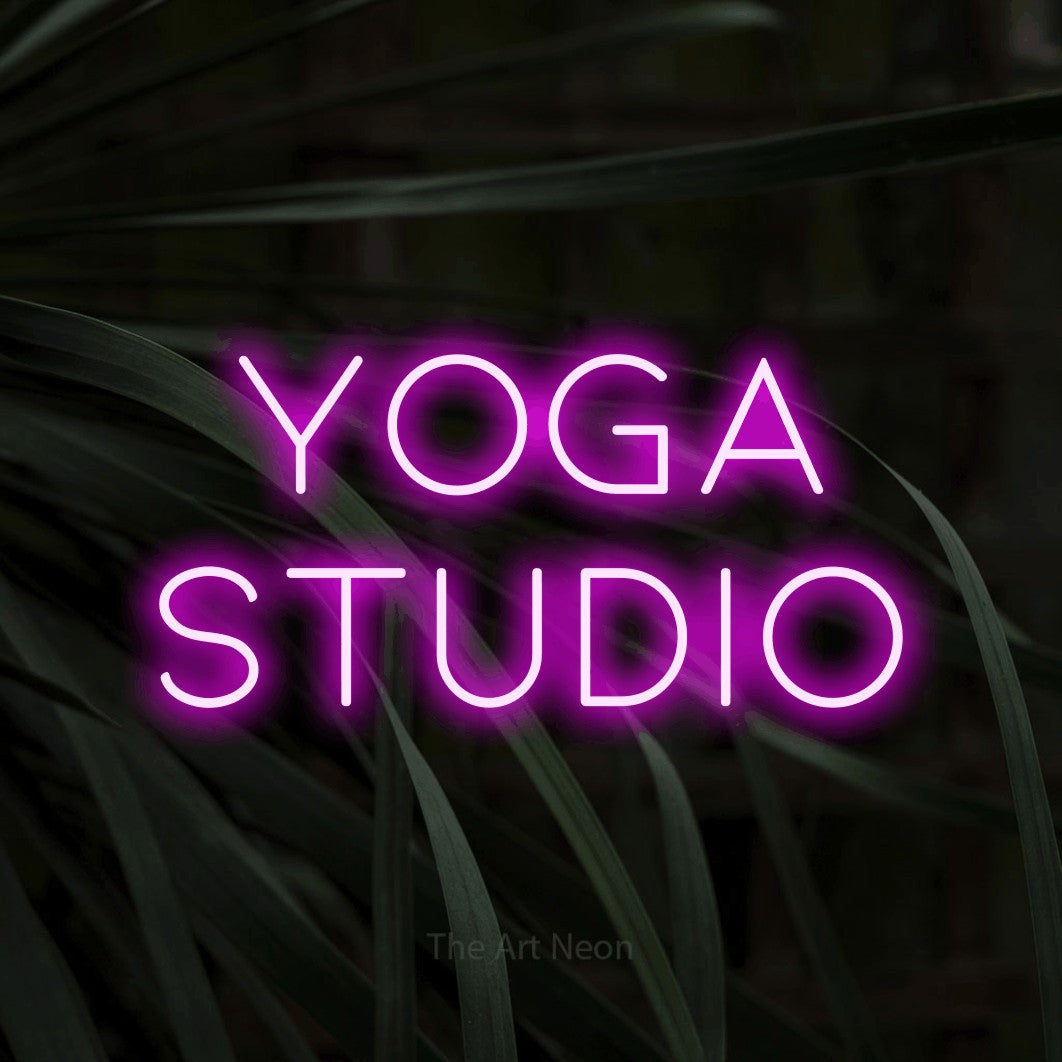 Pink LED neon sign reading "Yoga Studio" against dark tropical leaves for gym décor