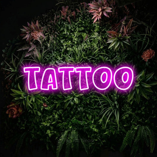 Pink outline-style LED neon sign reading "Tattoo" against a flowering garden wall for tattoo studio décor