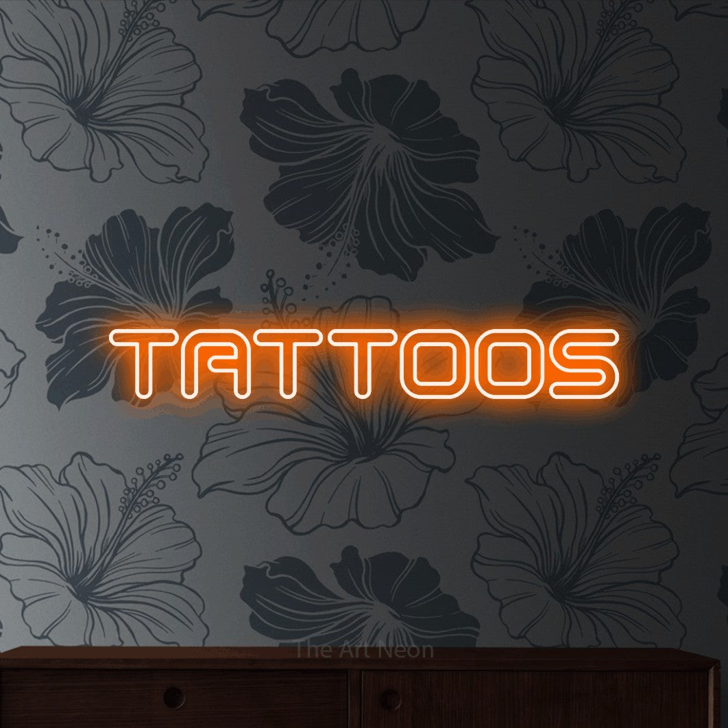 Orange outline-style LED neon sign reading "Tattoos" against grey floral wallpaper for tattoo studio décor