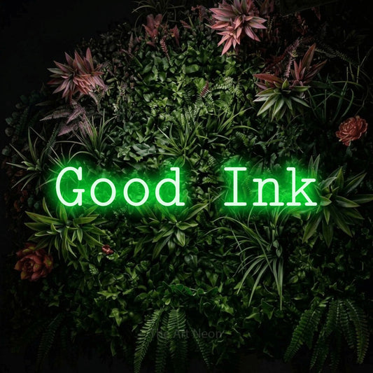 Green LED neon sign reading "Good Ink" against a flowering garden wall for tattoo studio décor