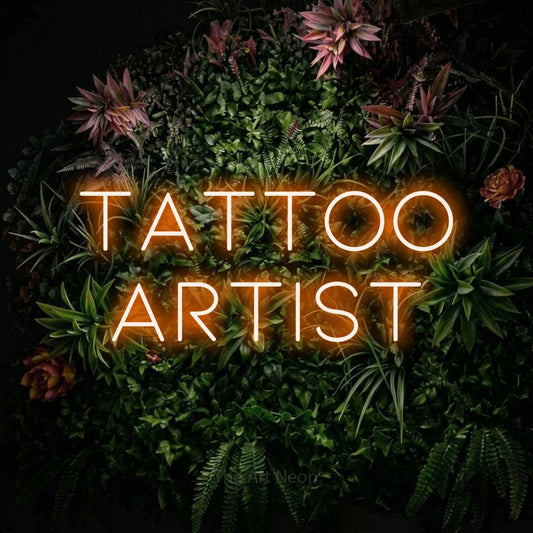 Orange LED neon sign reading "Tattoo Artist" against a flowering garden wall for tattoo studio décor