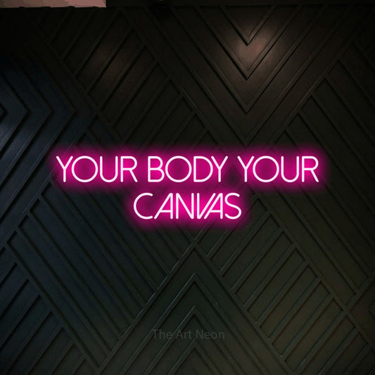 Hot pink LED neon sign reading "Your Body Your Canvas" against a dark geometric wood wall for tattoo studio décor