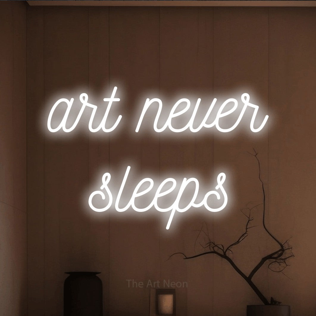 Cool white script-style LED neon sign reading "Art Never Sleeps" against a warm brown wall for tattoo studio décor