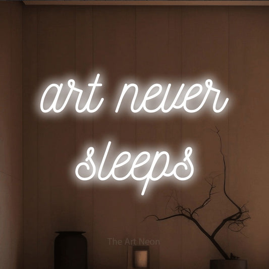Cool white script-style LED neon sign reading "Art Never Sleeps" against a warm brown wall for tattoo studio décor