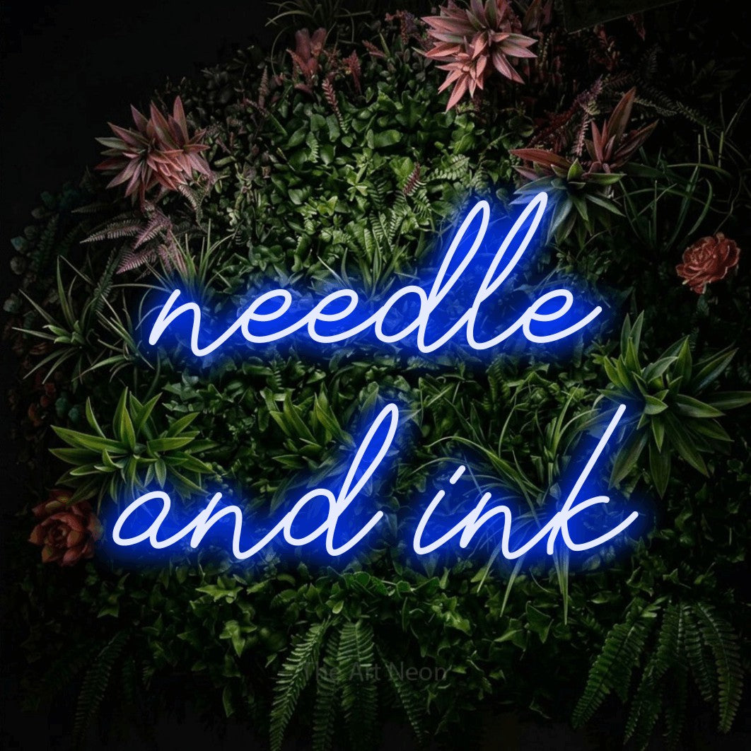Blue script-style LED neon sign reading "Needle and Ink" against a flowering garden wall for tattoo studio décor