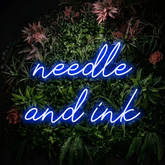Blue script-style LED neon sign reading "Needle and Ink" against a flowering garden wall for tattoo studio décor