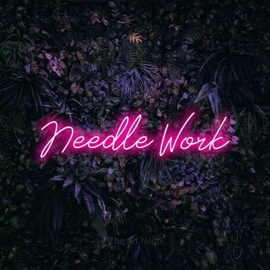 Hot pink script-style LED neon sign reading "Needle Work" against a purple floral wall for tattoo studio décor