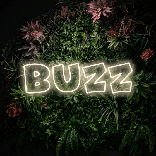 Warm white outline-style LED neon sign reading "Buzz" against a flowering garden wall for tattoo studio décor