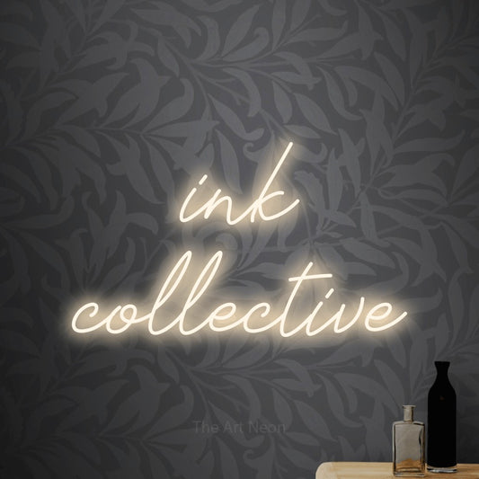 Warm white script-style LED neon sign reading "Ink Collective" against light grey floral wallpaper for tattoo studio décor