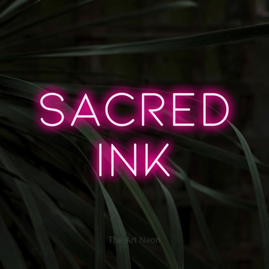 Hot pink LED neon sign reading "Sacred Ink" against dark tropical leaves for tattoo studio décor