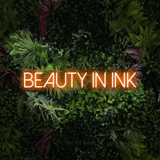 Orange LED neon sign reading "Beauty in Ink" against a lush garden wall with pink flowers for tattoo studio décor
