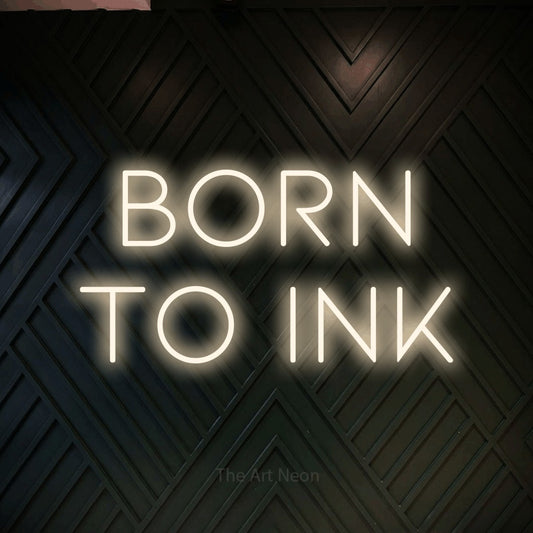 Warm white LED neon sign reading "Born to Ink" against a dark geometric wood wall for tattoo studio décor