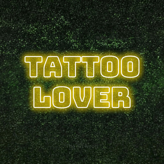 Yellow outline-style LED neon sign reading "Tattoo Lover" against a textured green moss wall for tattoo studio décor