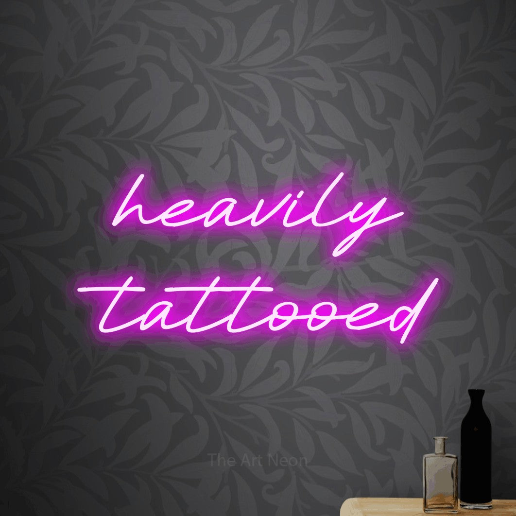 Pink LED neon sign reading "Heavily Tattooed" against light grey floral wallpaper for tattoo studio décor