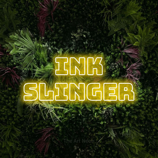 Yellow outline-style LED neon sign reading "Ink Slinger" against a lush garden wall with pink flowers for tattoo studio décor