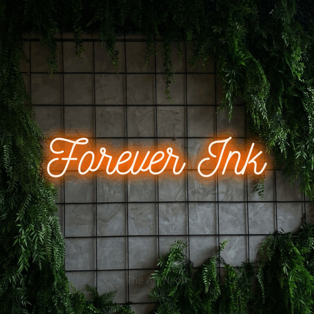 Orange script-style LED neon sign reading "Forever Ink" against a green grid wall with foliage for tattoo studio décor