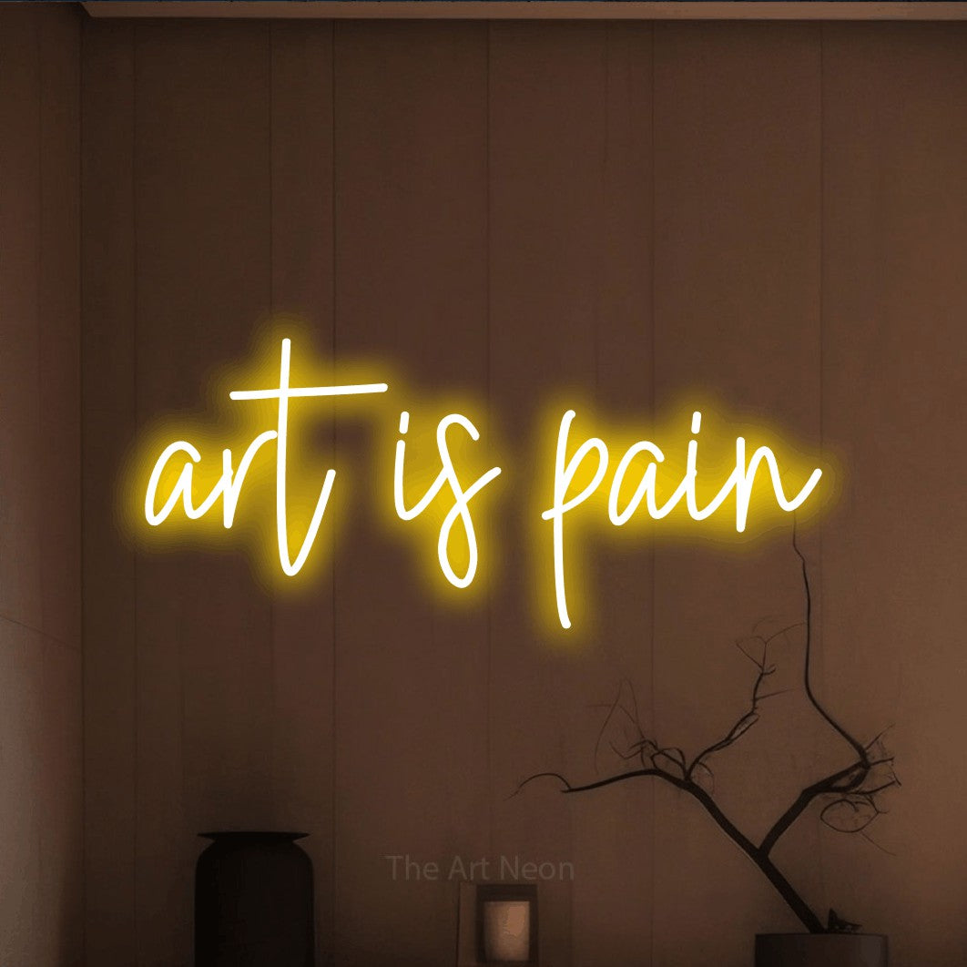 Yellow script-style LED neon sign reading "Art is Pain" against a warm brown wall for tattoo studio décor