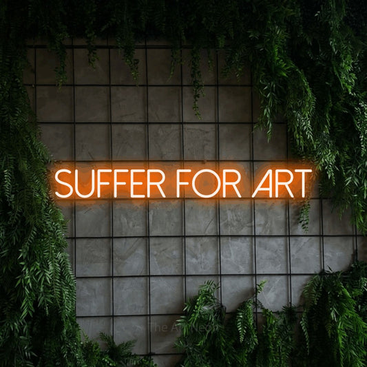 Orange LED neon sign reading "Suffer for Art" against a green grid wall with foliage for tattoo studio décor