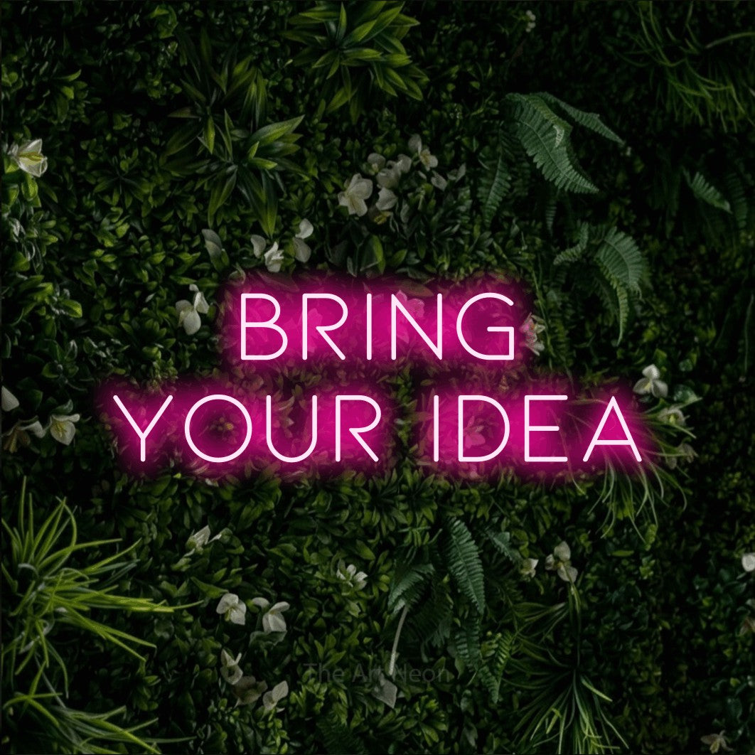 Hot pink LED neon sign reading "Bring Your Idea" against a leafy green wall for tattoo studio décor