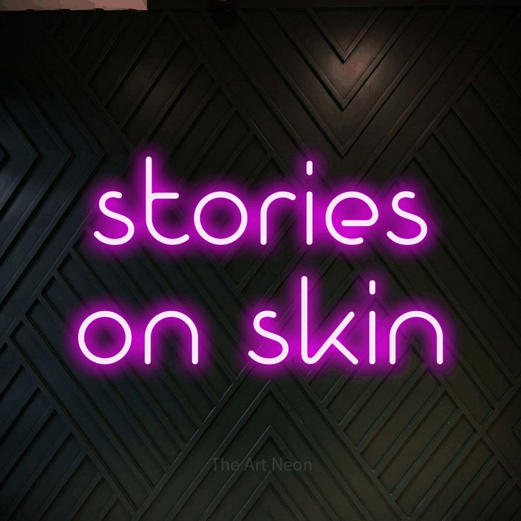 Pink LED neon sign reading "Stories on Skin" against a dark geometric wood wall for tattoo studio décor
