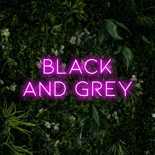 Pink LED neon sign reading "Black and Grey" against a leafy green wall for tattoo studio décor