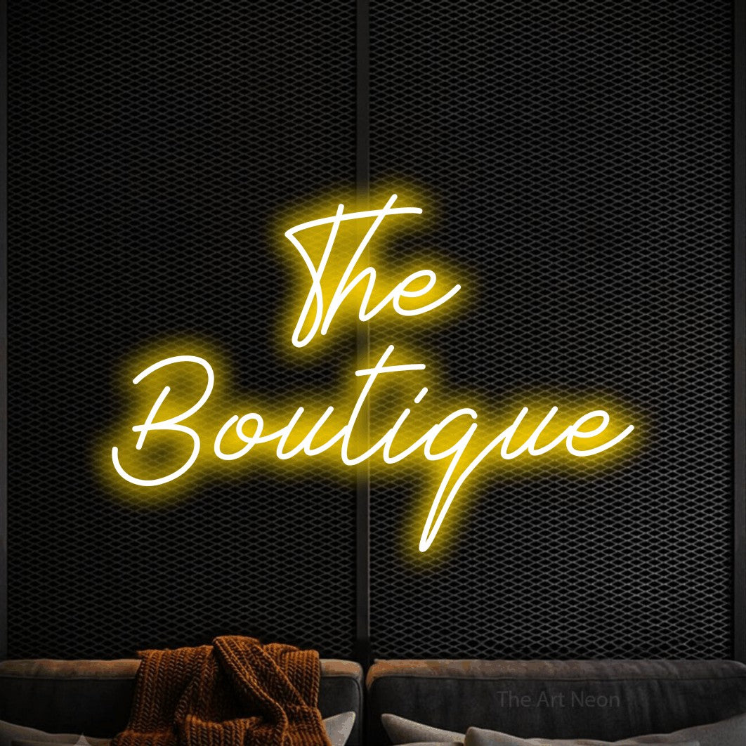 Yellow script-style LED neon sign reading "The Boutique" against a black textured wall