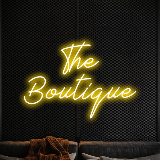 Yellow script-style LED neon sign reading "The Boutique" against a black textured wall