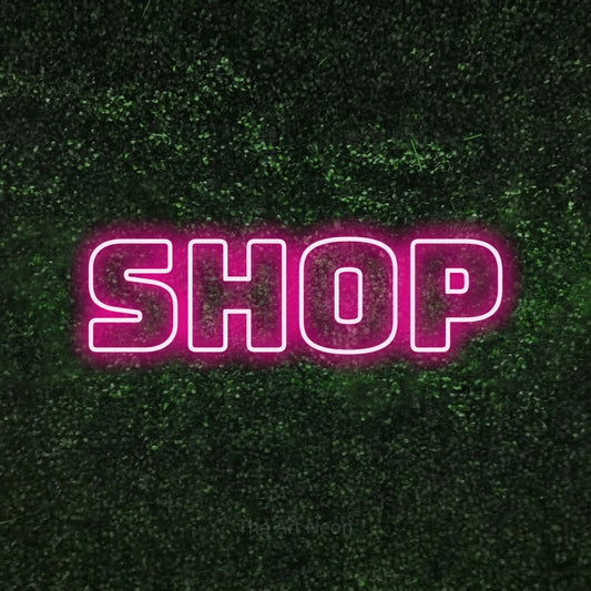 Hot pink outline-style LED neon sign reading "Shop" against a textured green moss wall