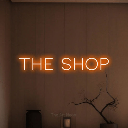 Orange LED neon sign reading "The Shop" against a warm brown wall