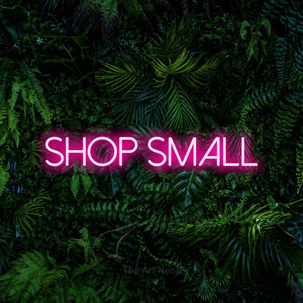 Hot pink LED neon sign reading "Shop Small" against a dense tropical foliage wall