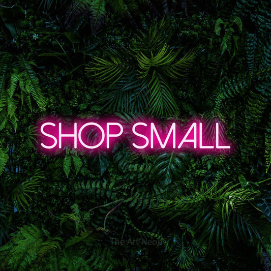 Hot pink LED neon sign reading "Shop Small" against a dense tropical foliage wall