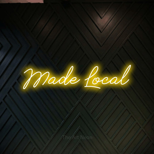 Yellow script-style LED neon sign reading "Made Local" against a dark geometric wood wall