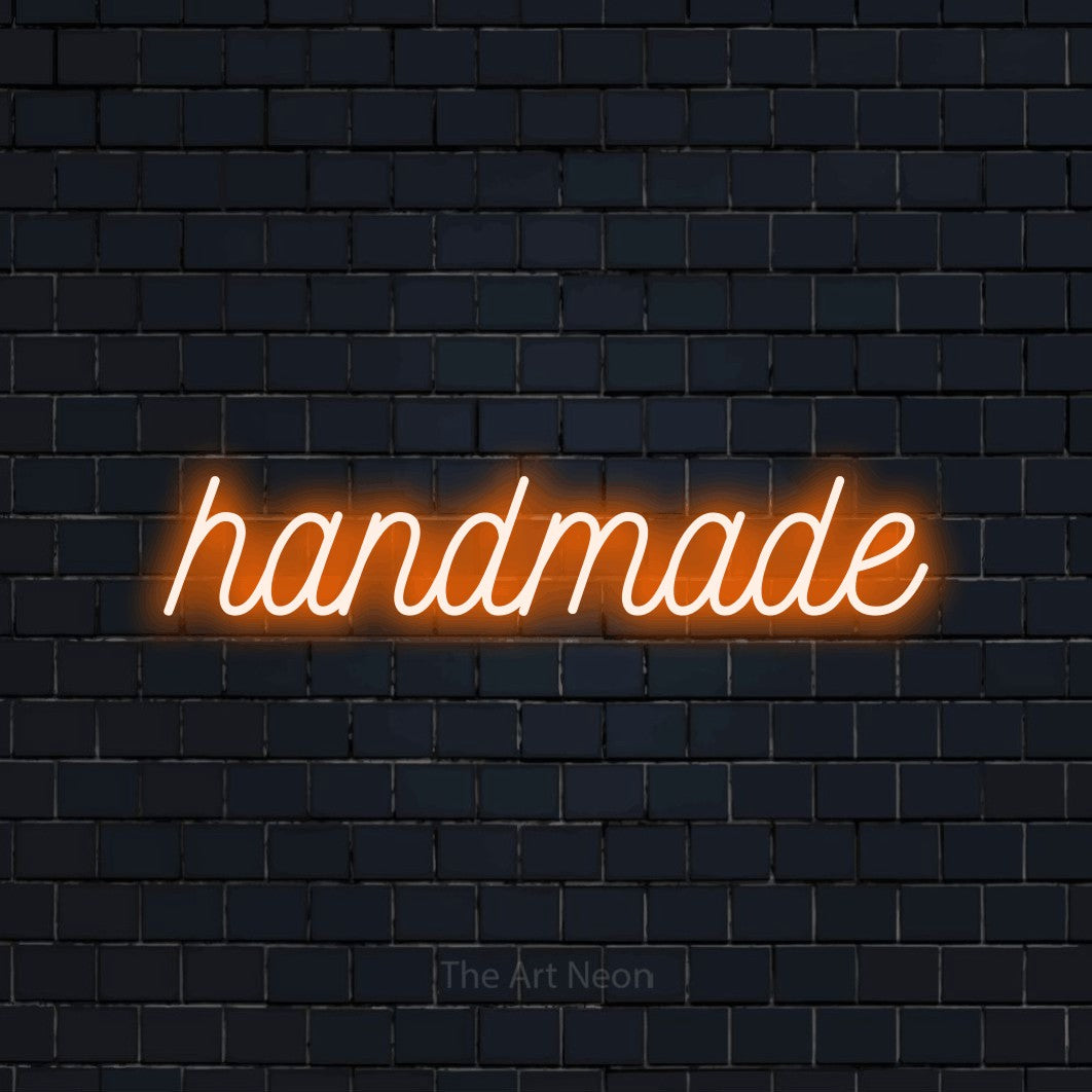 Orange script-style LED neon sign reading "Handmade" against a dark navy brick wall