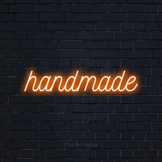 Orange script-style LED neon sign reading "Handmade" against a dark navy brick wall