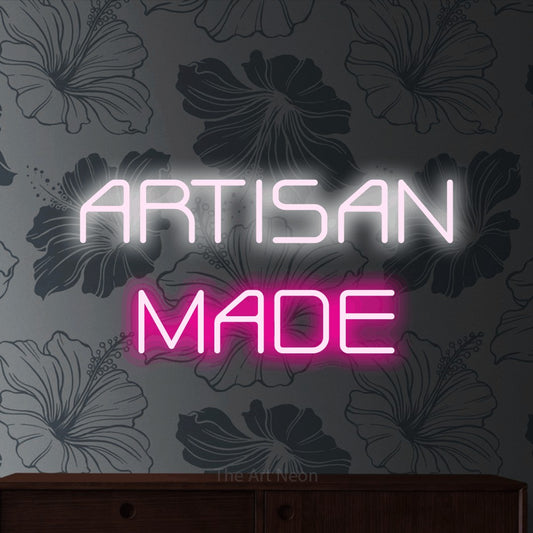 Hot pink and cool white LED neon sign reading "Artisan Made" against grey floral wallpaper