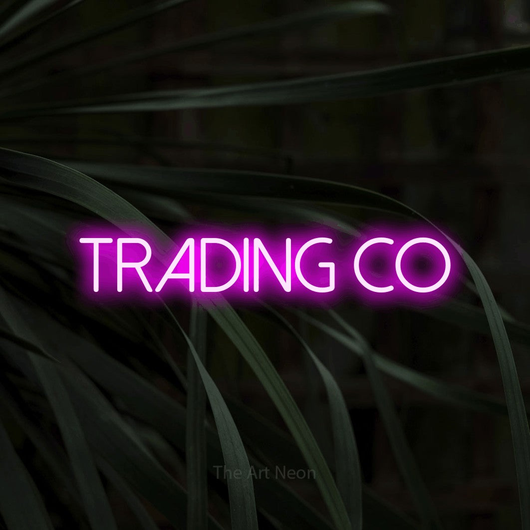 Pink LED neon sign reading "Trading Co" against dark tropical leaves