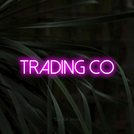 Pink LED neon sign reading "Trading Co" against dark tropical leaves