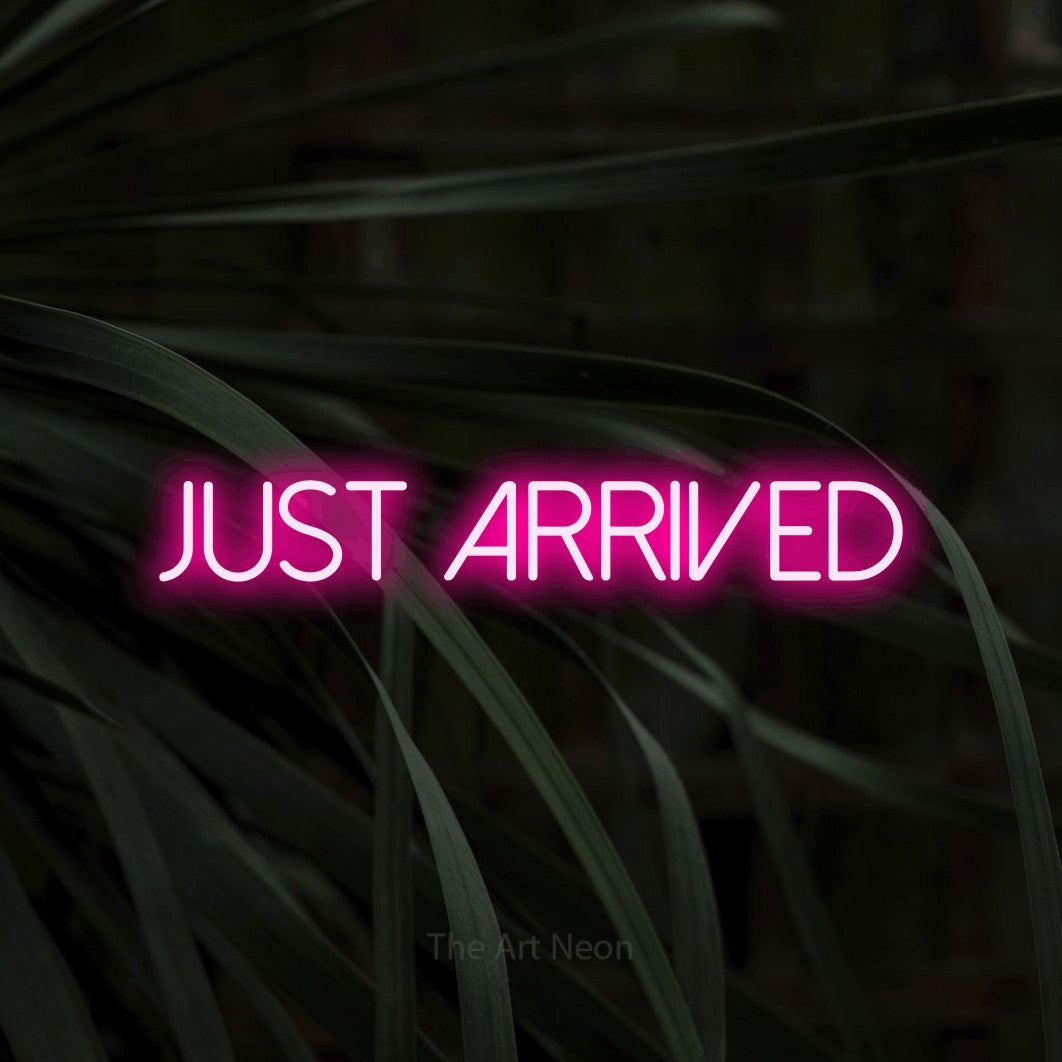 Hot pink LED neon sign reading "Just Arrived" against dark tropical leaves