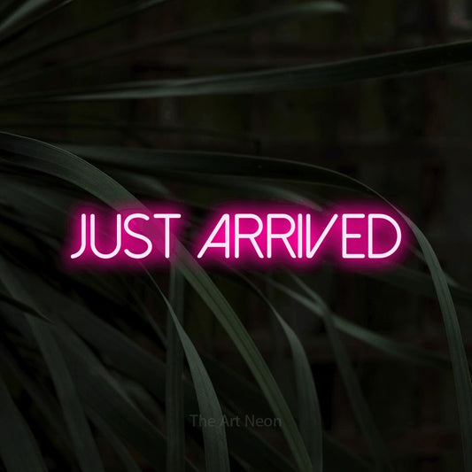 Hot pink LED neon sign reading "Just Arrived" against dark tropical leaves