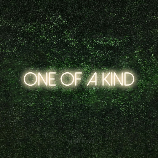 Warm white LED neon sign reading "One of a Kind" against a textured green moss wall