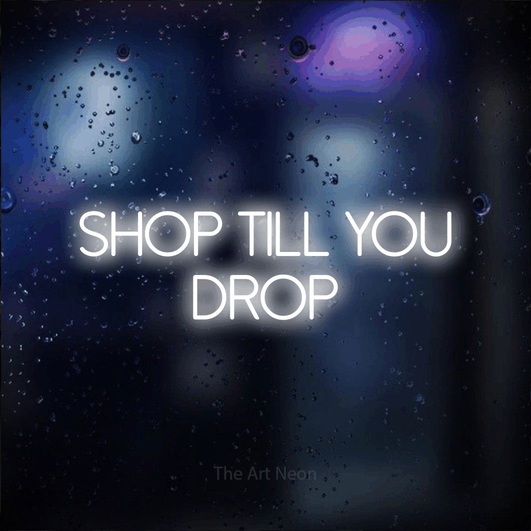 Cool white LED neon sign reading "Shop Till You Drop" against a dark blue bokeh background